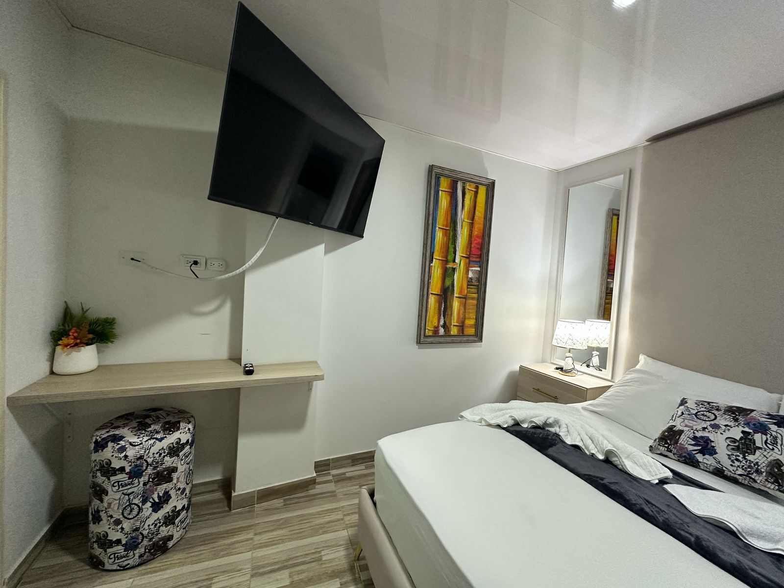 Una camera d'albergo con un letto, una scrivania, una sedia, una televisione a parete e un quadro appeso.