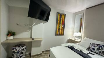 Una camera d'albergo con un letto, una scrivania, una sedia, una televisione a parete e un quadro appeso.