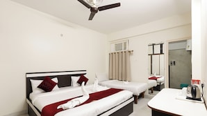 A hotel room with a large bed, a smaller bed, a desk with a kettle, and a ceiling fan. - BALAJI HOMESTAY VARANASI (Varanasi)