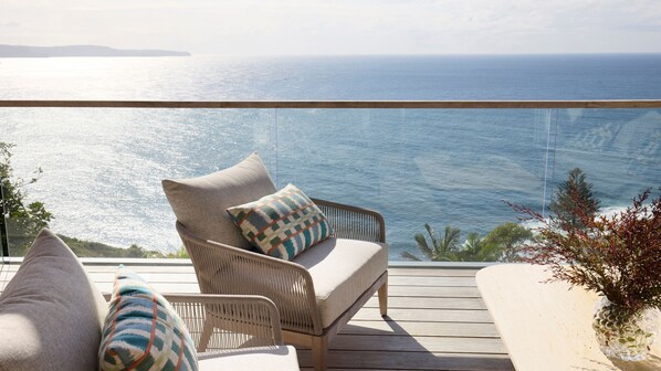 Um deck de madeira com móveis de vime e vista para o mar.