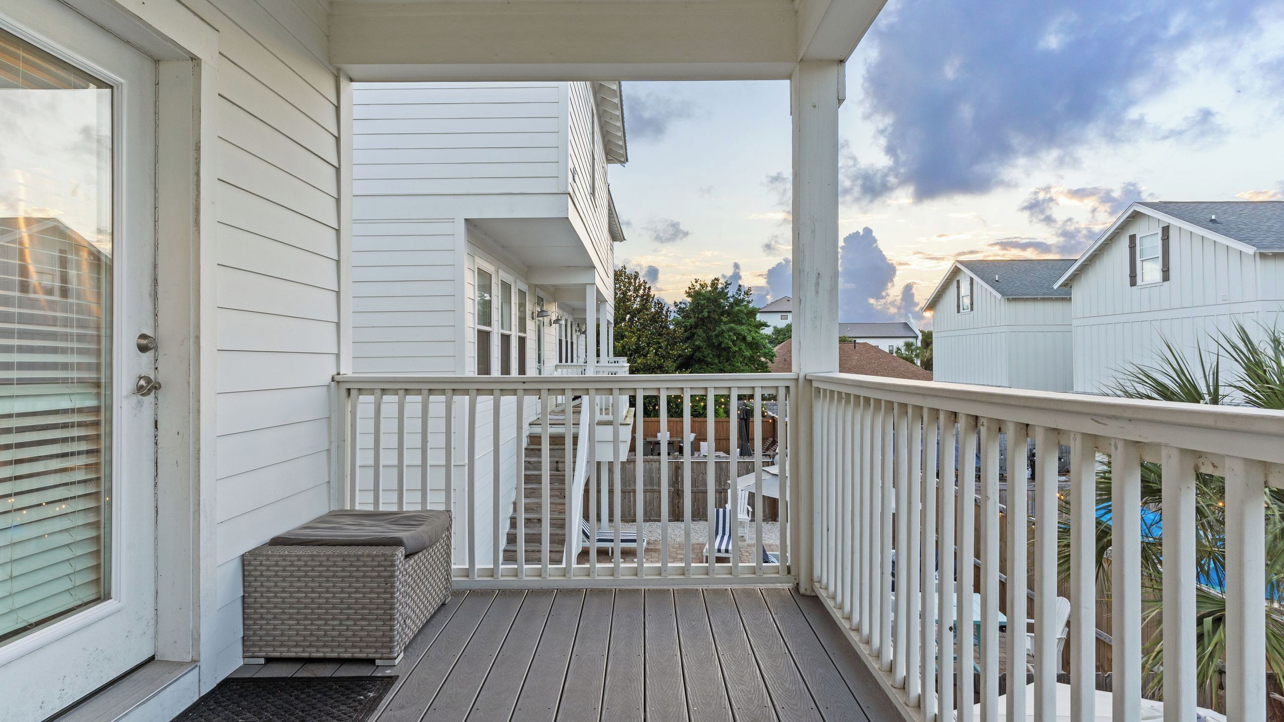 Een houten terras met een witte balustrade, een klein zitgedeelte en uitzicht op omliggende huizen.