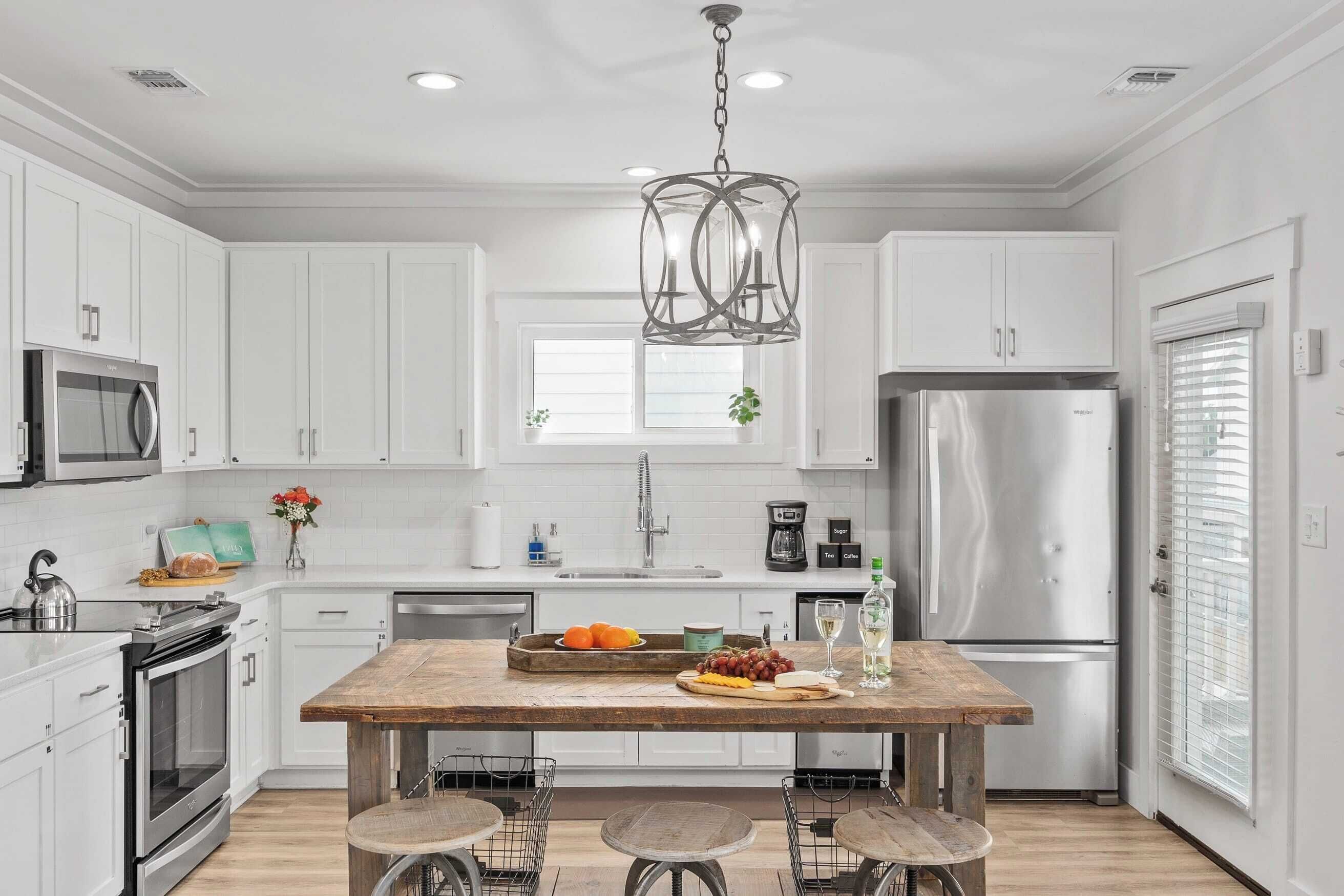 Una cocina moderna con armarios blancos, electrodomésticos de acero inoxidable, una isla de madera y taburetes de bar.