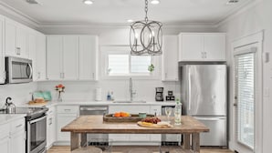 Une cuisine moderne avec des meubles blancs, des appareils en acier inoxydable, un îlot central en bois et un luminaire suspendu.