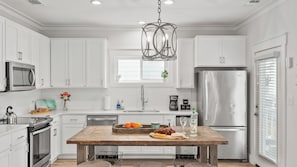 A modern kitchen with white cabinetry, stainless steel appliances, a wooden island, and a hanging light fixture.