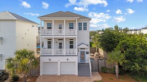 A two-story building with a front garage, a balcony on the second floor, and a small front yard with palm trees.