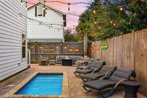 A backyard with a swimming pool, lounge chairs, a fire pit, and string lights. - Pool, Firepit, Near Miramar Beach Access Blue Surf Lane by Avantstay (Miramar Beach)