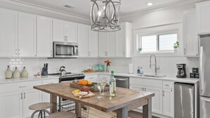 Une cuisine moderne avec des meubles blancs, des appareils en acier inoxydable, un îlot central en bois doté d’une planche à découper et un luminaire suspendu.