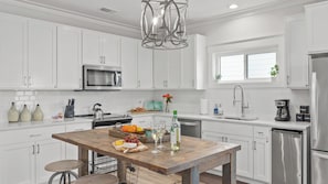 A modern kitchen with white cabinets, stainless steel appliances, a wooden island with a cutting board, and a hanging light fixture. - Pool, Firepit, Near Miramar Beach Access Blue Surf Lane by Avantstay (Miramar Beach)