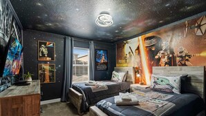Ein Schlafzimmer mit zwei Betten, Star Wars-Dekoration, einem Holztisch und einer galaxiengemusterten Decke.