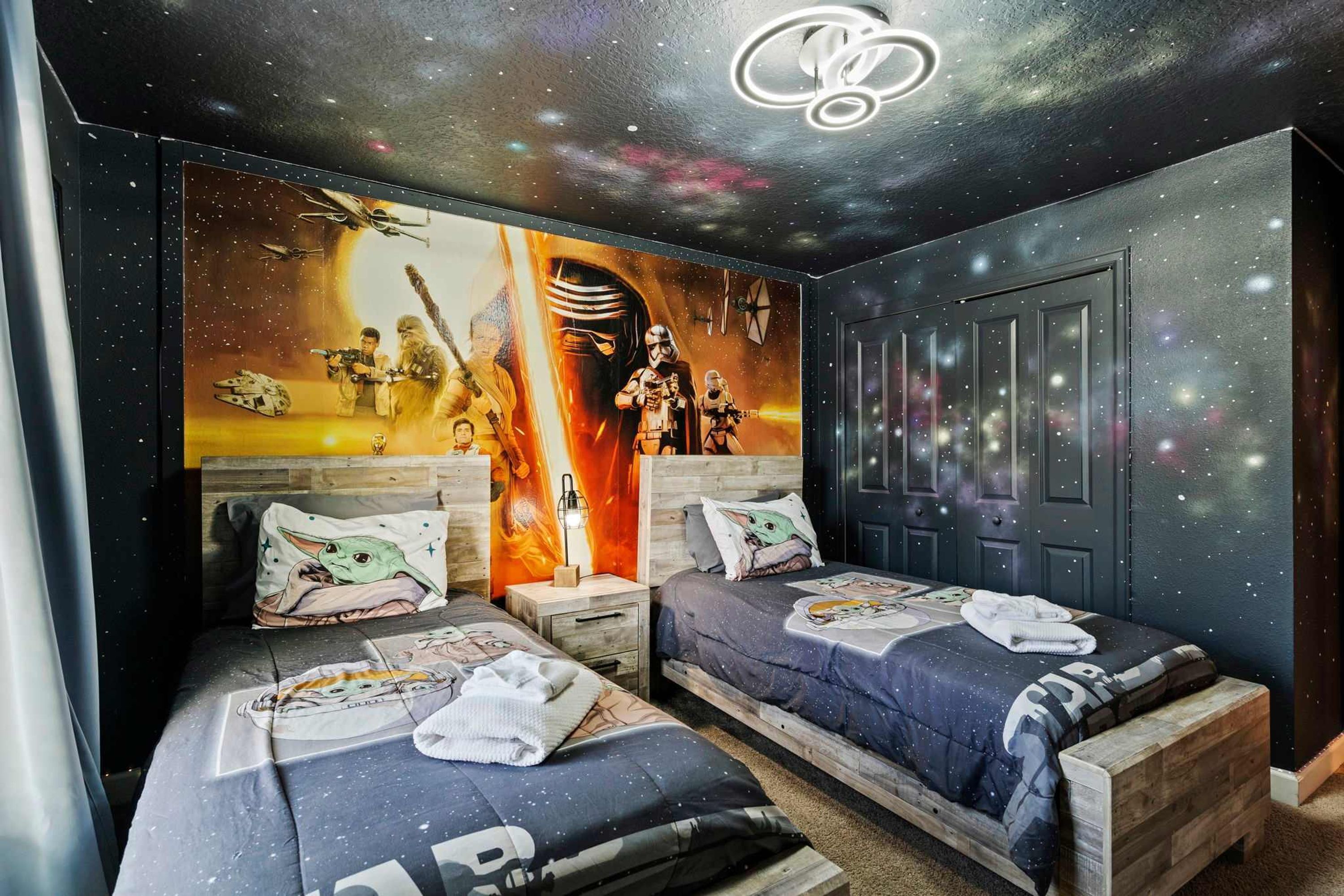 Un dormitorio con dos camas, un mural con temática galáctica y un techo estrellado.