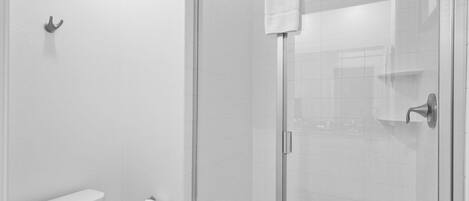 Un baño moderno con cabina de ducha de vidrio, inodoro y perchero.