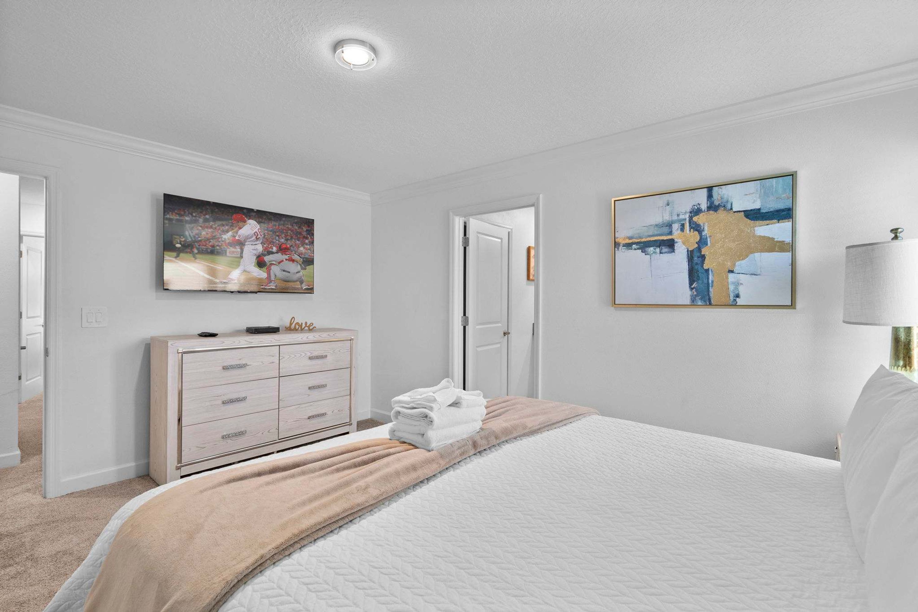 Una habitación de hotel con cama, cómoda, un cuadro y una lámpara.