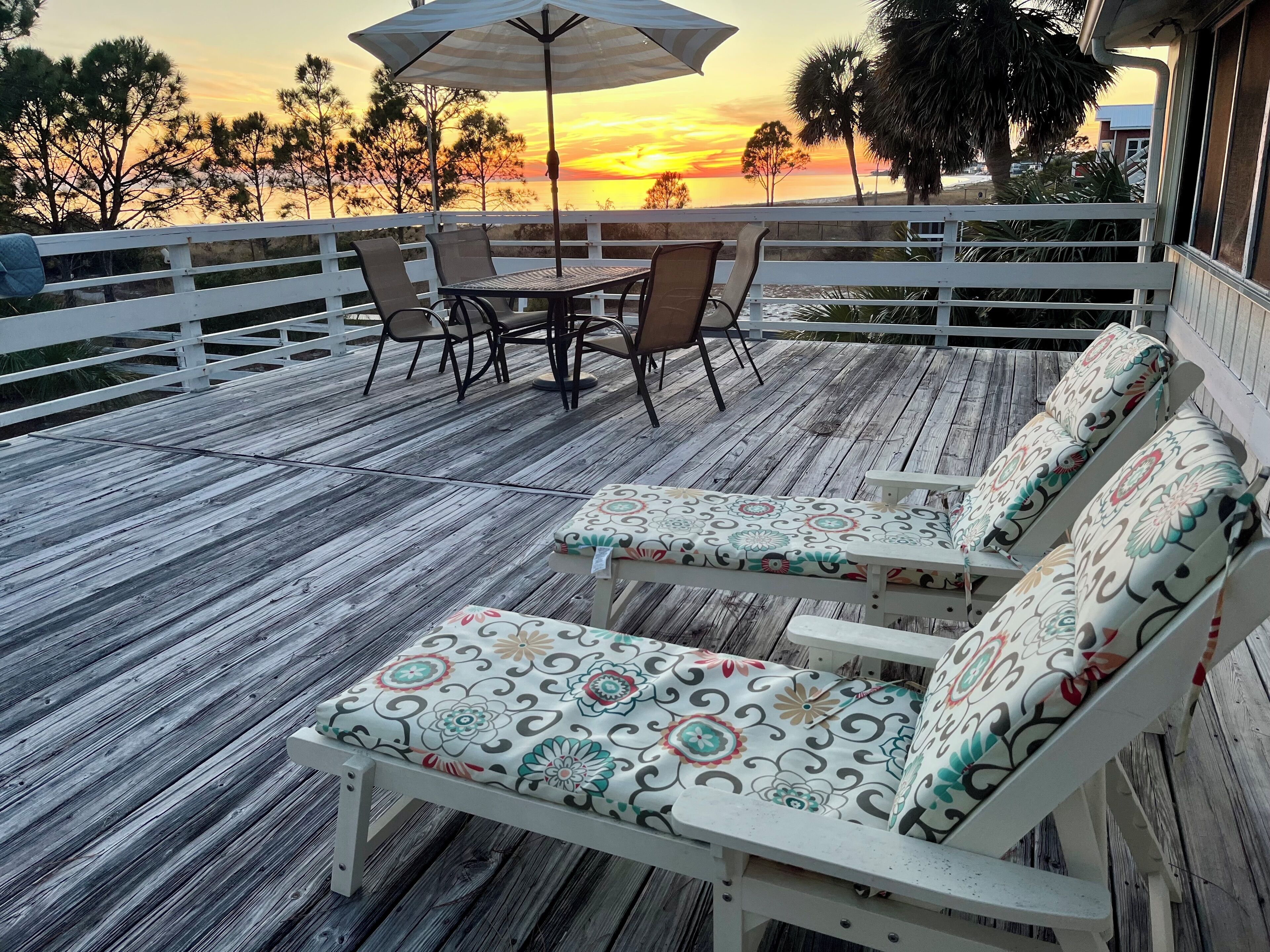 A wooden deck with outdoor furniture, including a table and chairs, and a bench with floral cushions.