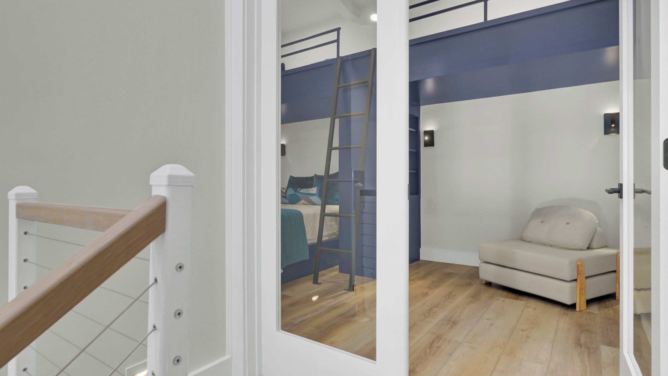 Ein Zimmer mit einem Etagenbett, einer Klapptreppe, einer Schlafcouch und Holzboden.