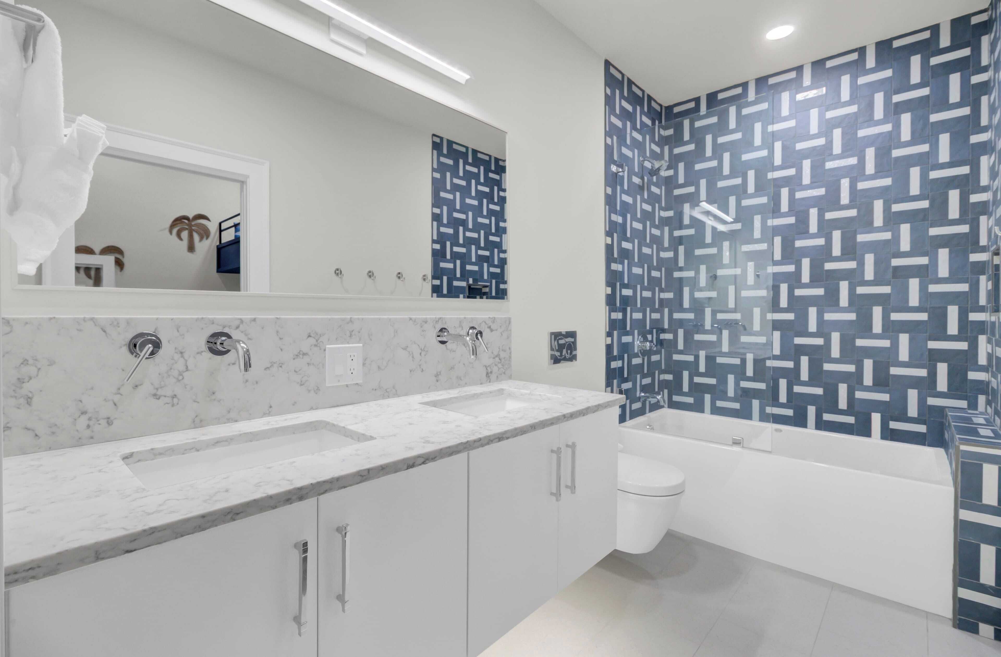 A modern bathroom with a marble countertop, a large mirror, a white toilet, and a bathtub.