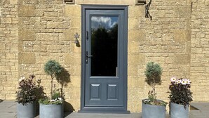 A stone building with a dark grey door, potted plants on either side, and a small bell above the door. - Walnut Farm, Kingscote, Cotswolds - Unique farm stay (Kingscote)