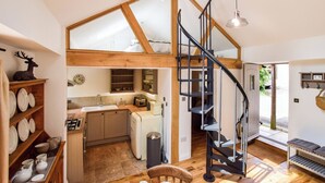 A spacious loft with a high ceiling, exposed wooden beams, a kitchen area, and a spiral staircase. - Walnut Farm, Kingscote, Cotswolds - Unique farm stay (Kingscote)