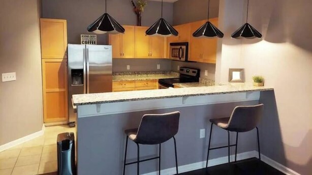 Una cucina moderna con isola centrale, sgabelli da bar, illuminazione a sospensione e un frigorifero con un cartello.