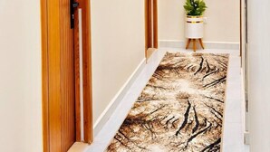 Un couloir avec des portes en bois, un panneau indiquant le numéro de la porte, un tableau encadré et une plante en pot.