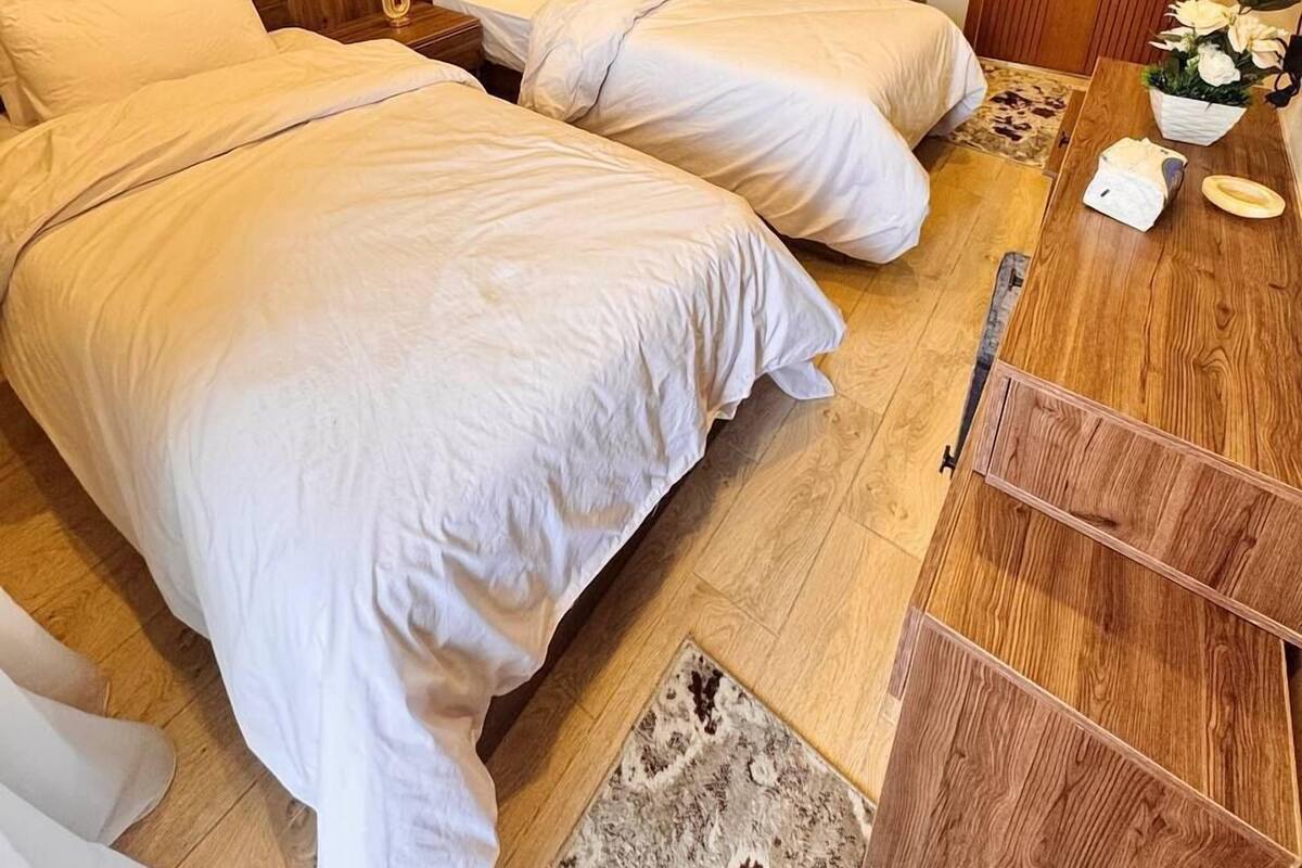 A hotel room with two beds, a wooden headboard, a mirror, a wooden dresser, and a small rug.