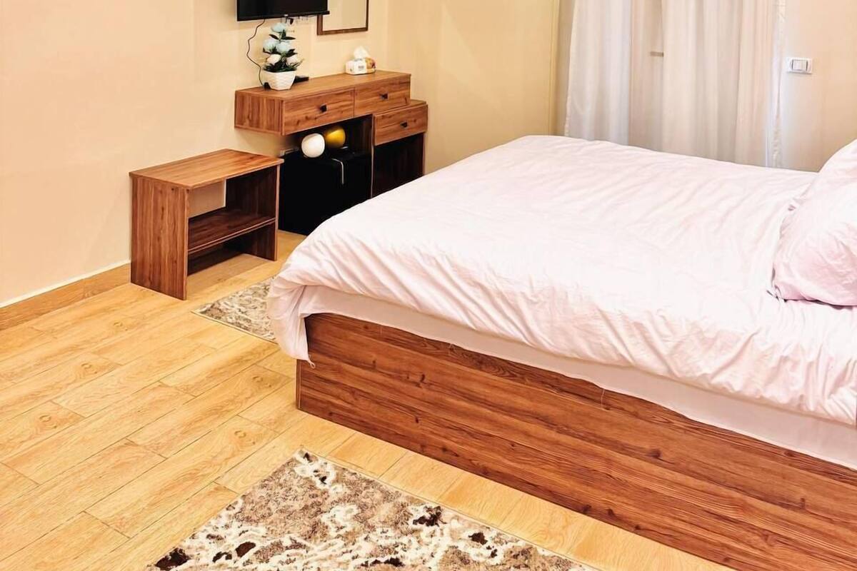 A modern bedroom with a wooden bed, a bedside table, a TV, and a ceiling with hanging balloons.