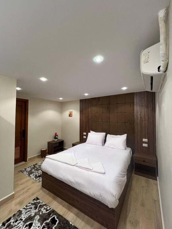 A modern bedroom with a large bed, wooden headboard, and a built-in air conditioning unit.