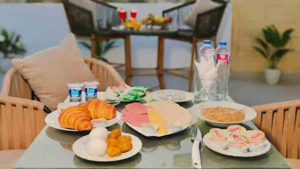Une table dressée pour le petit-déjeuner, avec des croissants, du jambon et des viennoiseries, donnant sur un plan d’eau.