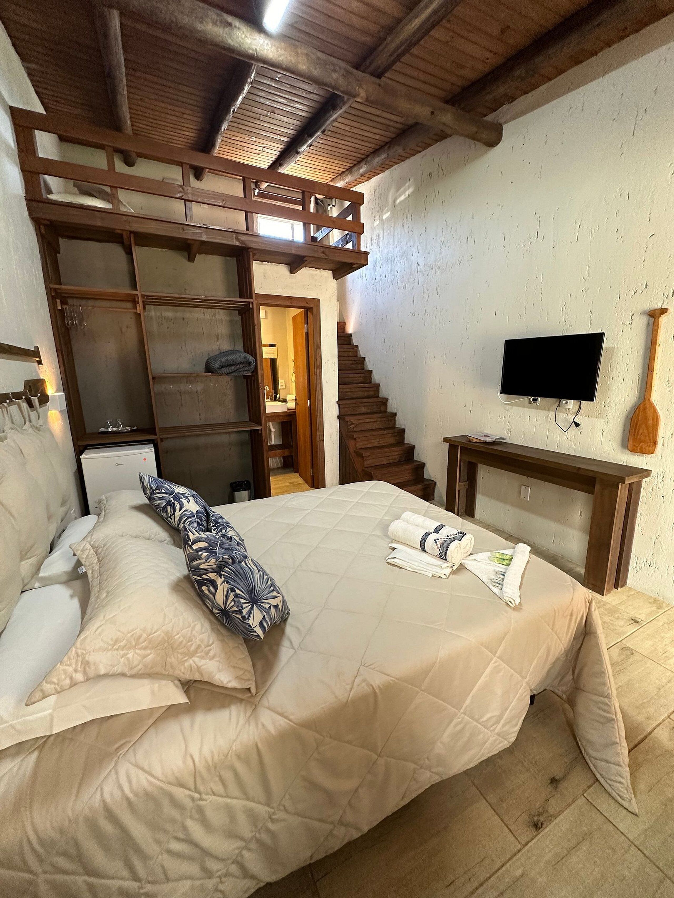 Una camera da letto con un letto, un armadio in legno, una televisione e una scala che conduce a un'altra stanza.