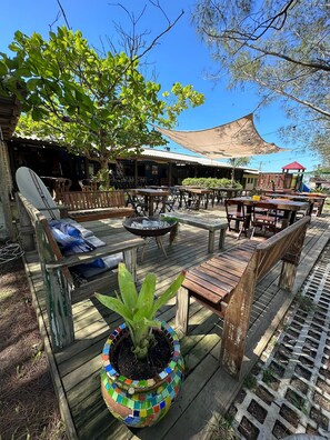 An outdoor seating area with wooden tables and chairs, a colorful mosaic planter, and a barbecue grill. - Pousada Cardoso Surf Camping - Laguna - SC (Laguna)