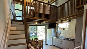 A spacious interior with a wooden staircase leading to a balcony, a kitchen area, and seating with a view of the outdoors. - Pousada Cardoso Surf Camping - Laguna - SC (Laguna)