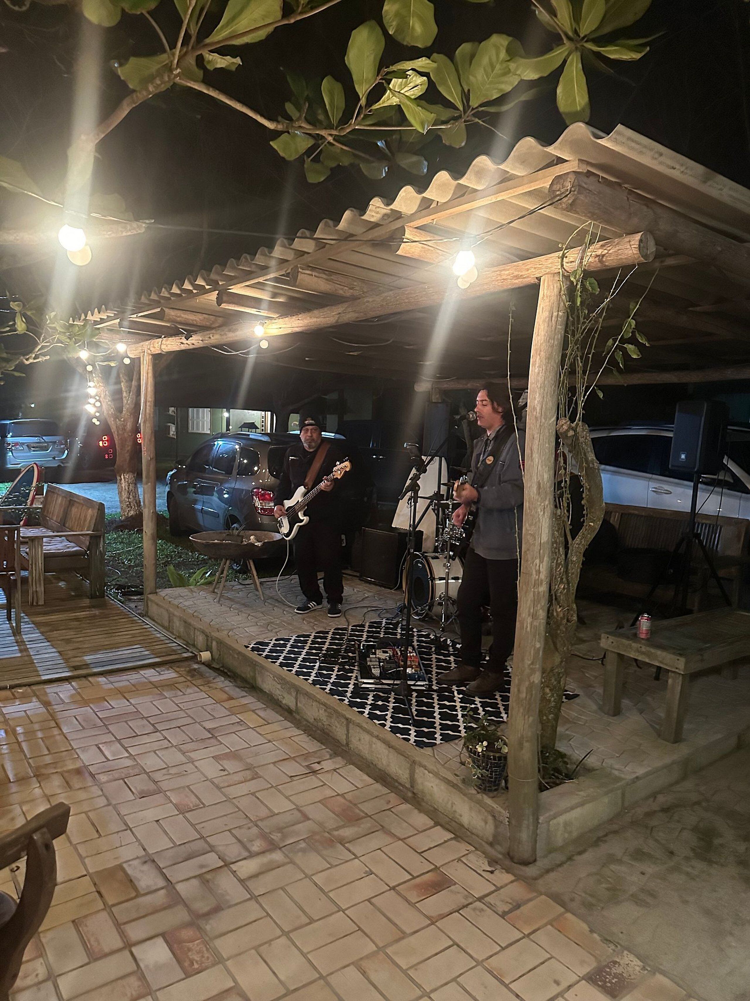 Un área de patio al aire libre con un pérgola de madera, un escenario con instrumentos musicales y un suelo de ladrillo.