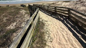 A wooden boardwalk leading to a beach with sandy dunes and ocean waves in the background. - Pousada Cardoso Surf Camping - Laguna - SC (Laguna)