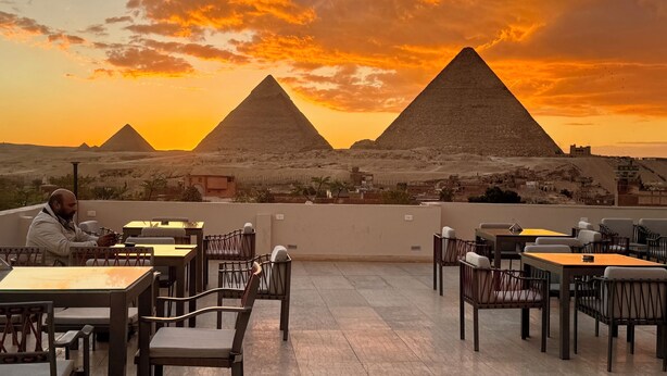 A terrace with tables and chairs, overlooking pyramids and a desert landscape. - Pyramids Secret (Giza Governorate)