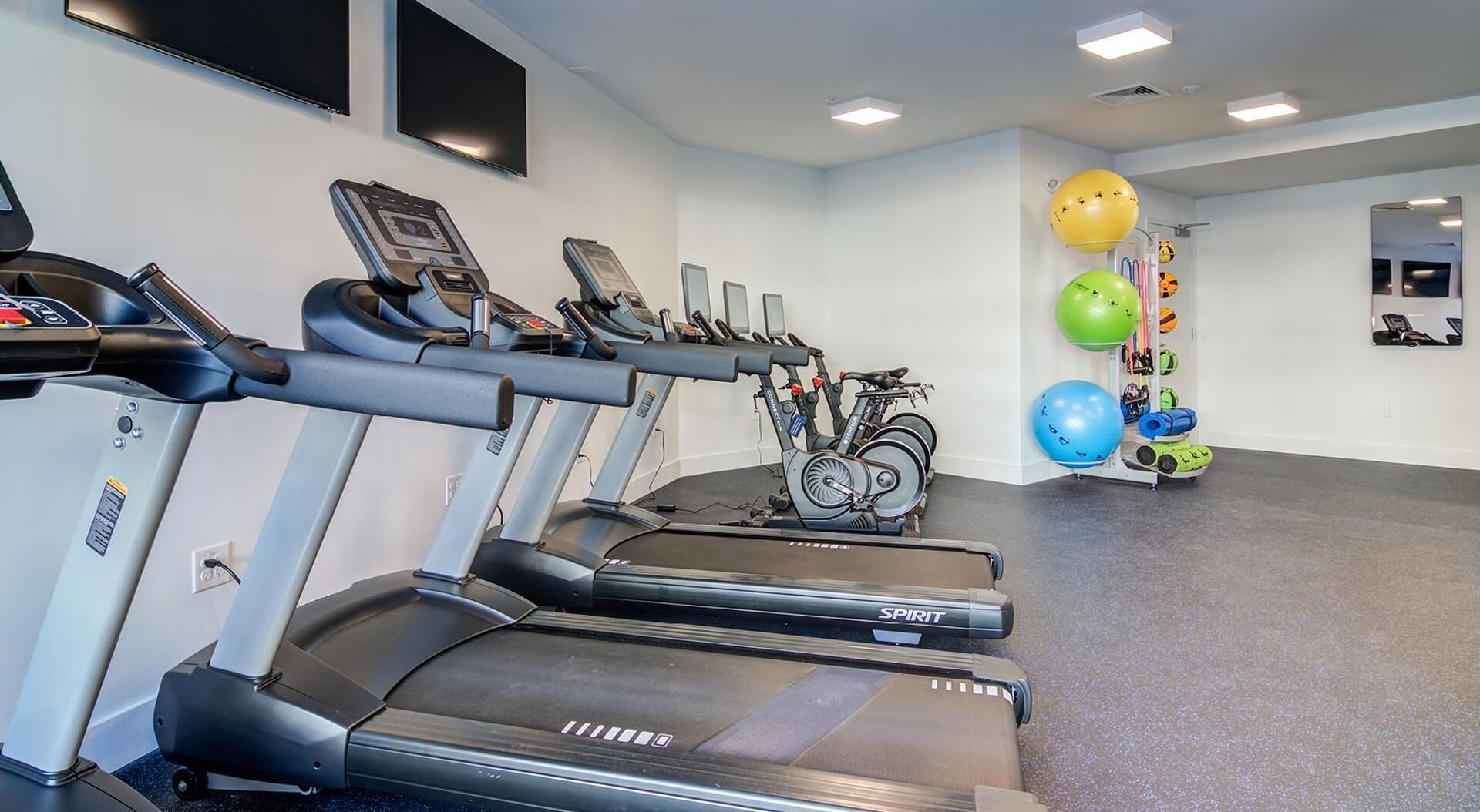 A gym with treadmills, stationary bikes, and exercise balls.