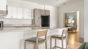 A modern kitchen with white cabinetry, a granite countertop, and two bar stools. - Landing | Incredible 1BD, Clubhouse, Pool (Decatur)