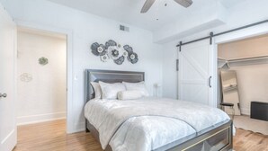 A bedroom with a bed, a ceiling fan, a wall-mounted decorative piece, and a sliding door closet. - Carson Flats Apt #6 | 1BR • Near BOK• OSU Med•Dtwn (Tulsa)