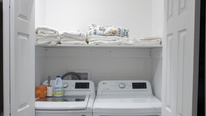 A laundry room with two washing machines and a shelf above containing folded towels.