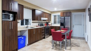 A modern kitchen with dark wooden cabinets, stainless steel appliances, and a dining area with red chairs.