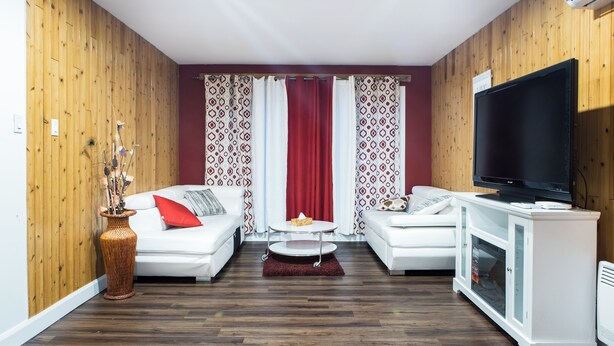 A modern living room with two white sofas, a round coffee table, a large flat-screen TV, and a decorative vase.