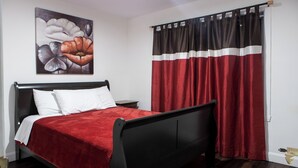 A bedroom with a black bed frame, red bedding, a white pillow, and a large floral artwork on the wall.