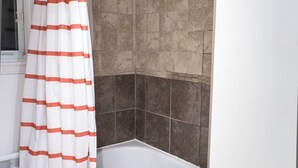 A bathroom with a white bathtub, a red towel, and a striped shower curtain.