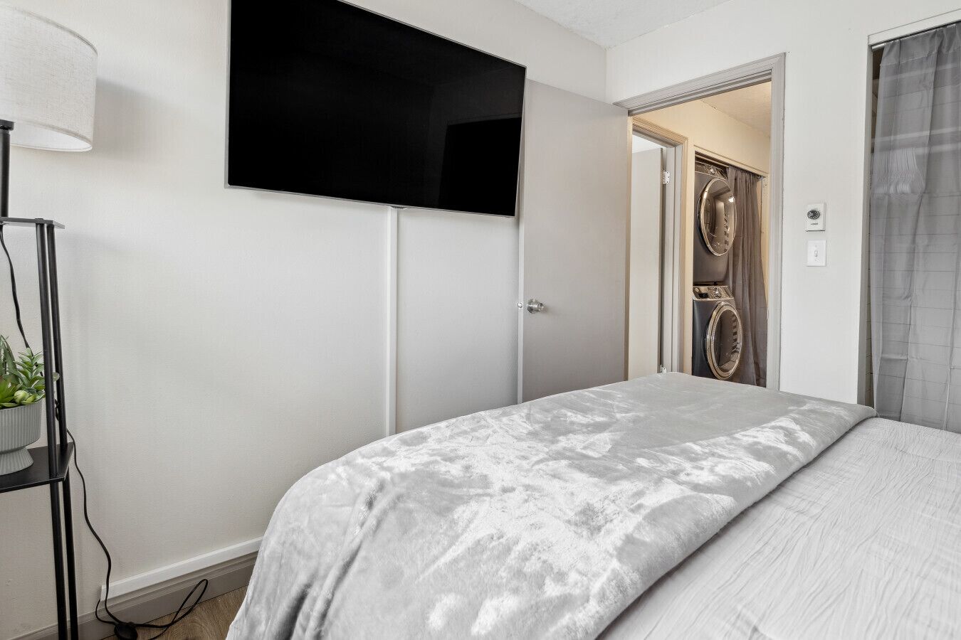 Un dormitorio con cama, televisor montado en la pared, armario y puerta que da a un baño.