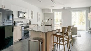 A modern kitchen with stainless steel appliances, a granite countertop island, and wooden chairs. - Landing | Incredible 1BD, Clubhouse, Pool (Decatur)