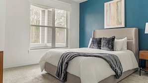 A bedroom with a large window, a bed with white and grey bedding, a blue accent wall, and a framed artwork above the bed. - Landing | Incredible 1BD, Clubhouse, Pool (Decatur)