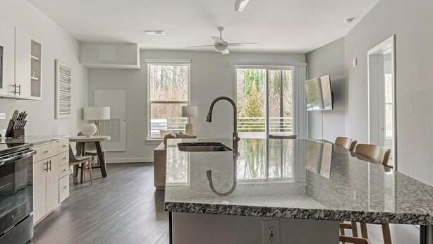 A modern kitchen with a large island, a dining area with chairs, and a TV mounted on the wall. - Landing | Incredible 1BD, Clubhouse, Pool (Decatur)