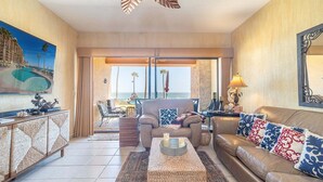 Una sala de estar con sofá, sillones, una mesita de centro y vista al océano a través de grandes puertas correderas.