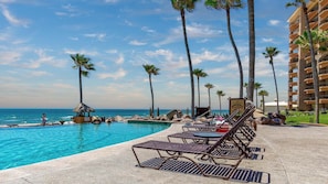 A pool area with lounge chairs, palm trees, and a building in the background.