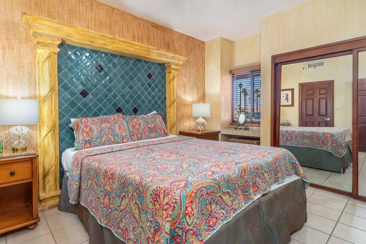 Une chambre à coucher avec une couvre-lit à motifs, une tête de lit en bois, une table de chevet avec une lampe et un miroir au mur.