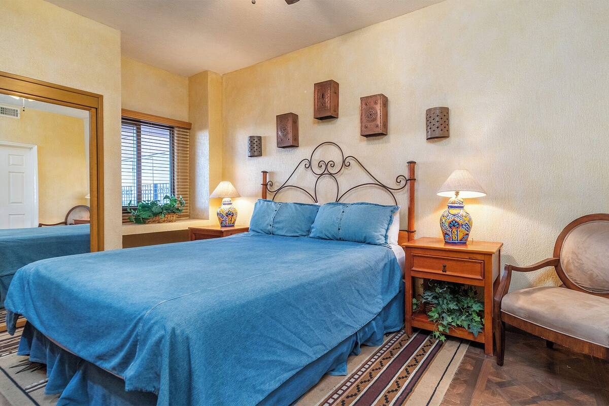 Une chambre à coucher avec un grand lit, deux tables de chevet avec des lampes, une chaise et un miroir.