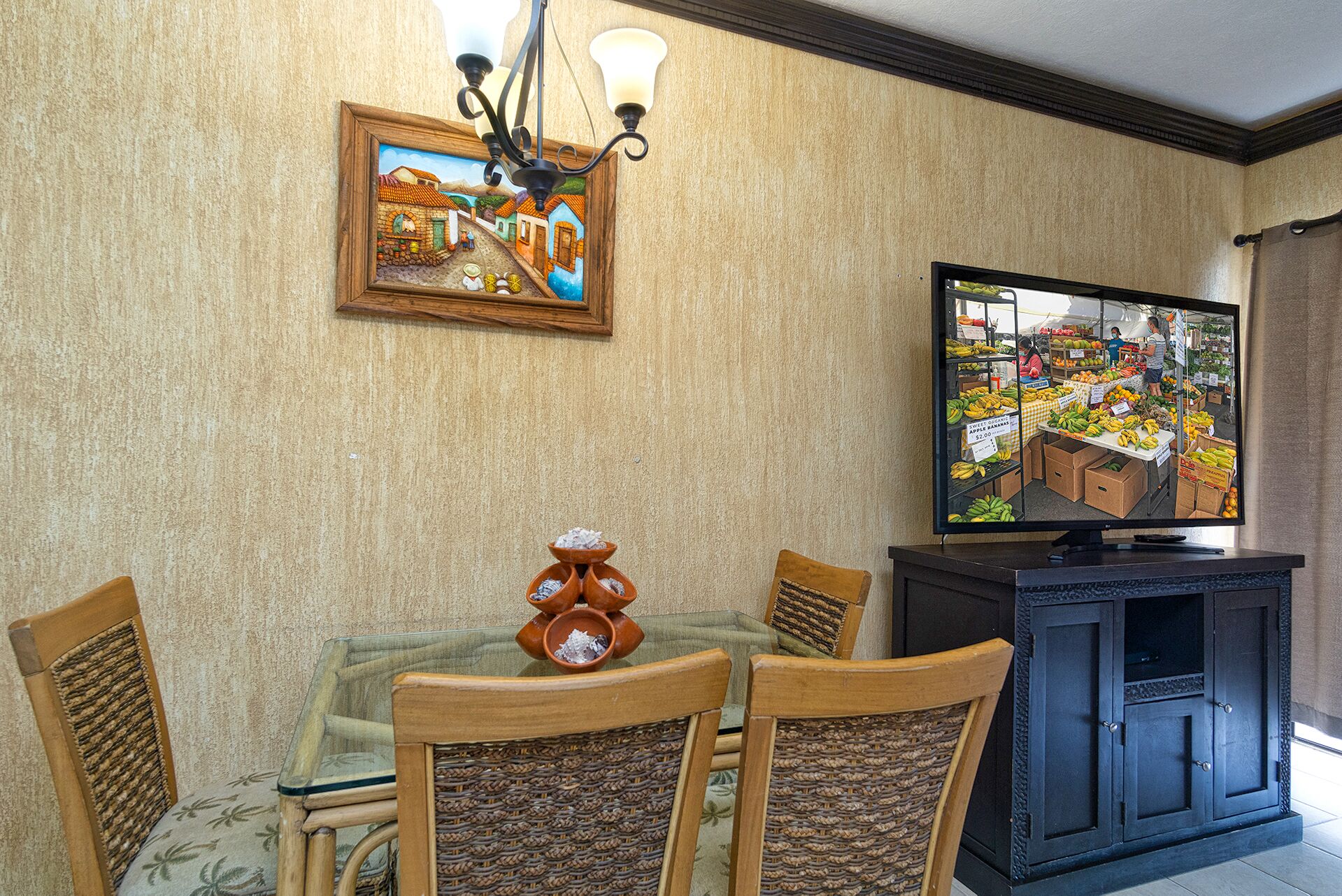 A dining area with a glass table, wooden chairs, a television, and a wall-mounted picture.